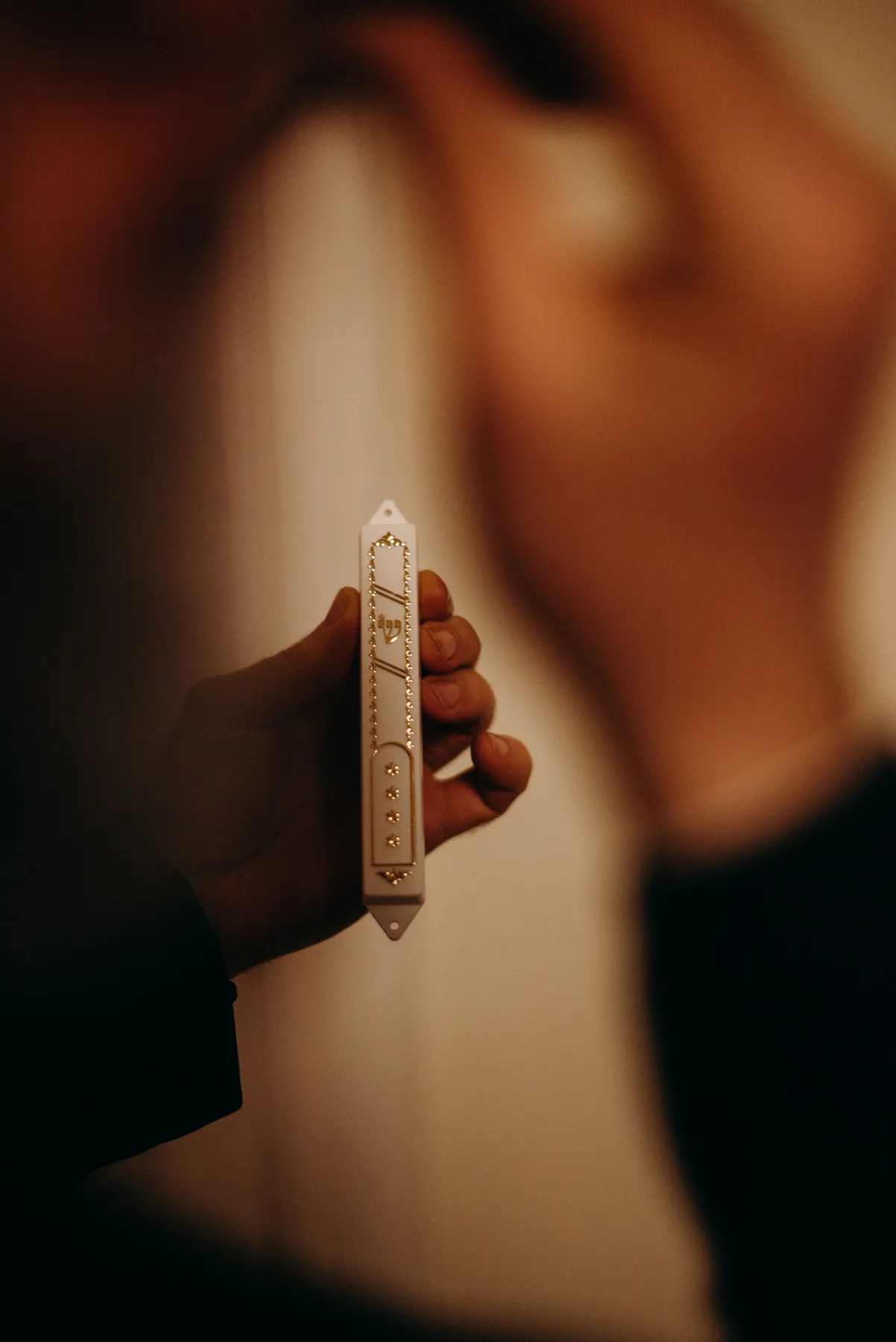 A hand holding a mezuzah in warm light